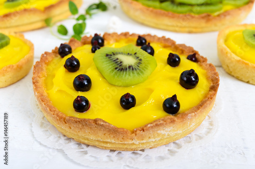 Tartlets, tartas from custard, kiwi and black currant on a white wooden background. Close up