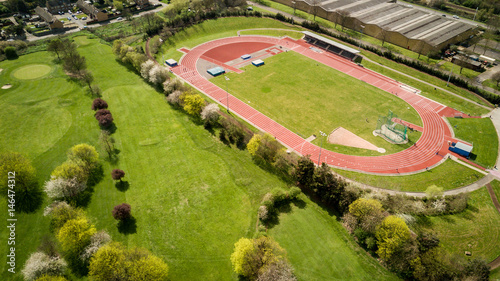 Track and field. Aerial view of athletes training on a North London running track set by a golf course on a bright sunny day.