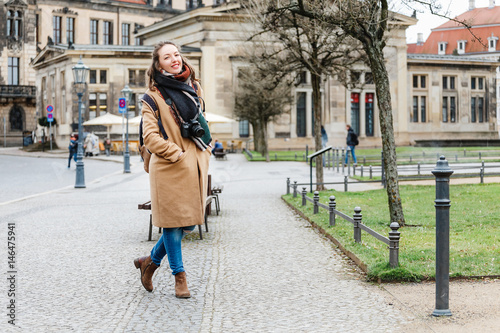 Hipster style girl on background of the old city of Dresden. A woman wearing warm coat, knitted scarf and photo camera