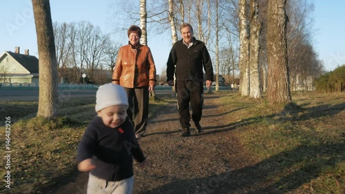 An attractive kid runs away from his grandparents in the park to his mother. A woman takes it and whirls in the rays of the setting sun
