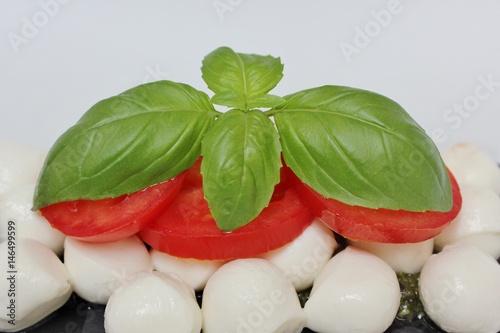 Italian Caprese salad with mini mozzarella balls, tomato, green pesto and basil