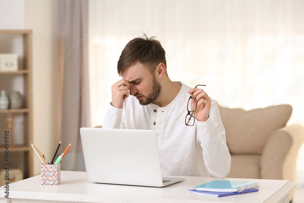 Young man with headache sitting at table with laptop Young man with headache sitting at table with laptop