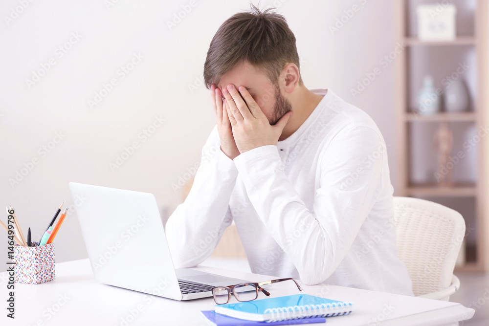 Young man with headache sitting at table with laptop Young man with headache sitting at table with laptop