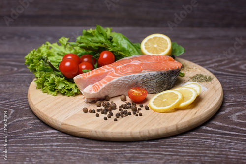 Raw salmon steaks on the wooden board. Lettuce leaves, spices, lemon slices on a wooden board. Woody background.