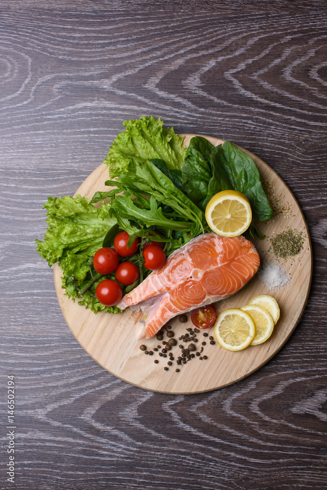 Raw salmon steaks on the wooden board. Lettuce leaves, spices, lemon slices on a wooden board. Woody background. view from above
