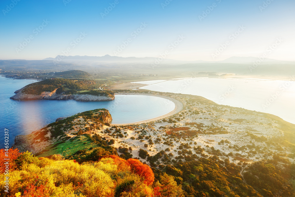 Amazing aerial landscape from Navarino castle ruins above colorful trees and over Voidokilia yellow sand pristine beach by Mediterranean sea, Peloponnese peninsula, Greece. Sunrise scenery, blue sky.