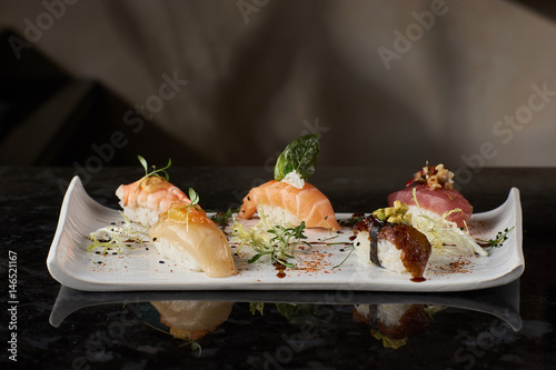 Sushi nigiri set on black marble background. Salmon, eel, prawn and tuna fish served on white plate with chopsticks.