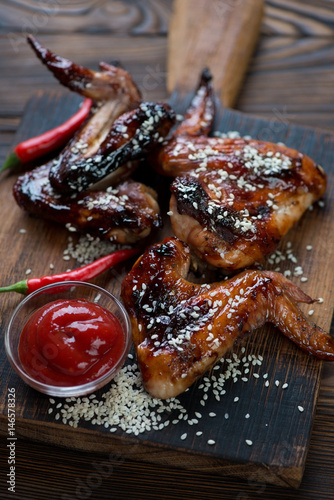 Close-up of barbecued chicken wings with sesame seeds and sauce, vertical shot, selective focus