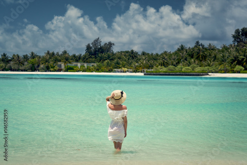 A girl in a white dress comes into the water. Maldives. Beach. Indian Ocean.
