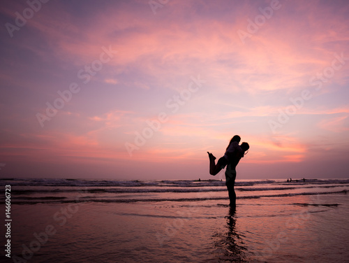 Couple kissing on the beach with a beautiful sunset in background  man lifting the woman