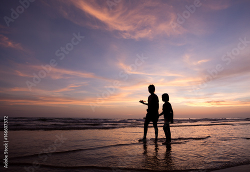 silhouette of mother and child walking on the tropical beach sunset background