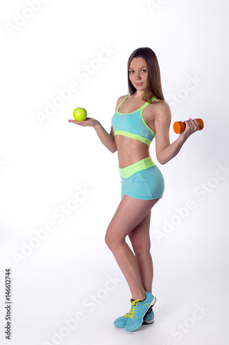 Slim fitness woman poses with apple and dumbbell
