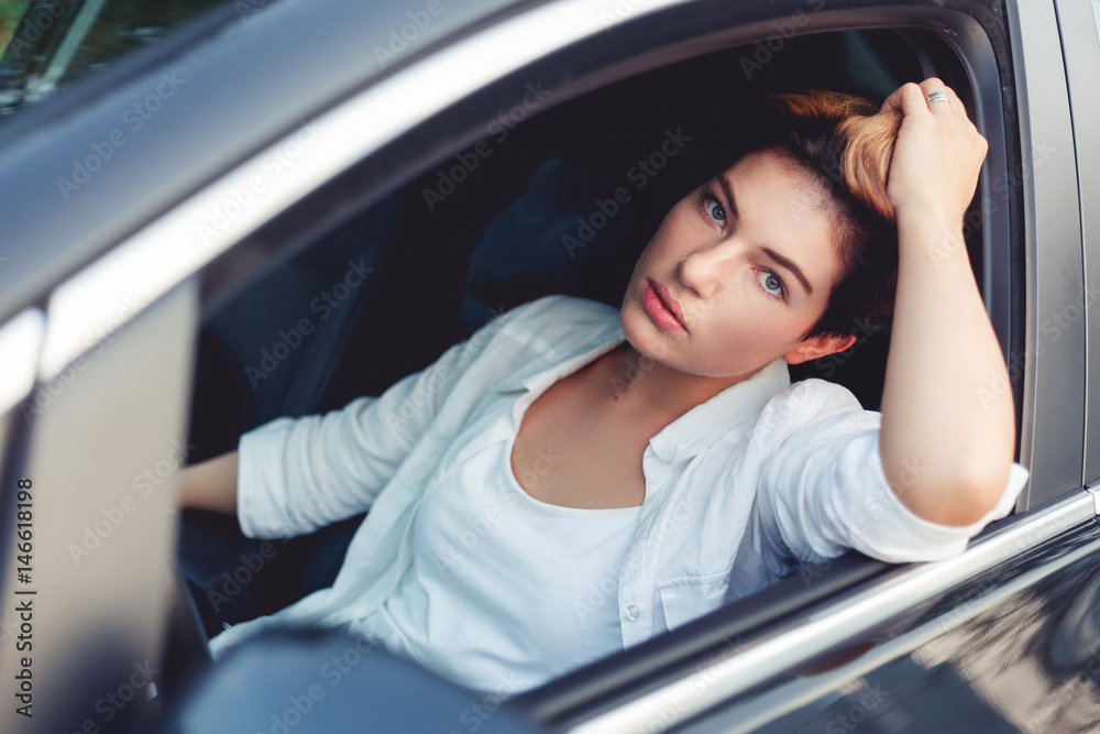 Pensive girl in white sitting at wheel of her car