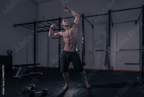 one young man, bodybuilder muscular shirtless, dark gym indoors