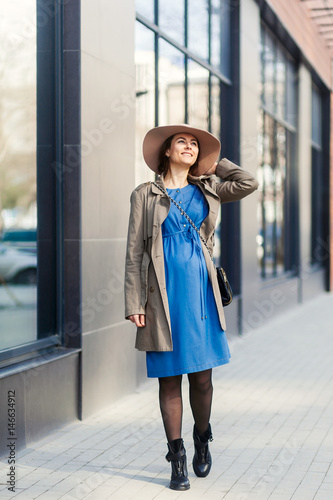 Fashion trends for pregnant women. Modern pregnant woman in blue comfortable dress and beige hat