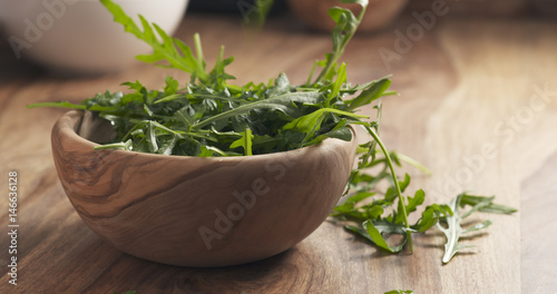 washed arugula leaves falling into the bowl on wooden table, 4k photo