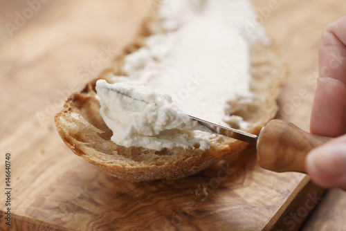 spreading ricotta cheese on fresh rustic bread, shallow focus