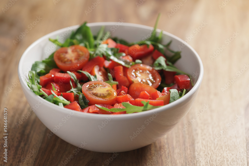 cherry tomatoes with arugula salad in white bowl on wooden table