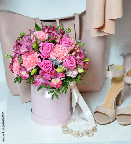 A beautiful bouquet of pink roses in a box for hats stands next to women's shoes and a handbag