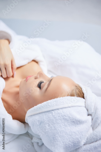 A woman in a bathrobe and a towel on her head lies on a bed