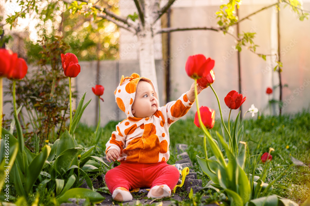cheerful little girl sitting in grass looking at tulips . kid plays outside. Happy child playing alone in spring garden