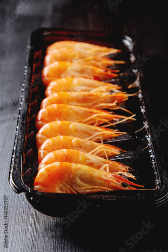 Fresh raw shrimps in a bowl on a wooden table. Eating seafood. Dark background.