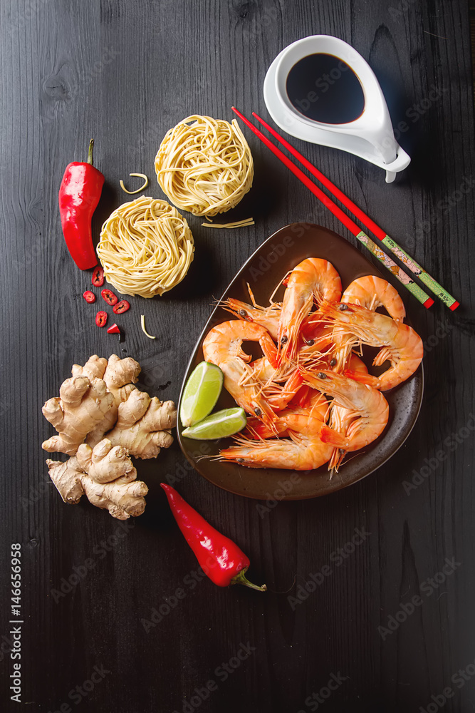Asia culture. Fresh raw shrimp, noodles, chili pepper, ginger, soy sauce in a bowl on a wooden table. Eating seafood. Dark background. Top view