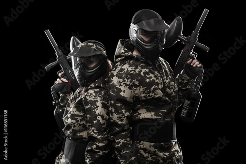 Heavily armed masked paintball soldier isolated on black background. Ad concept.