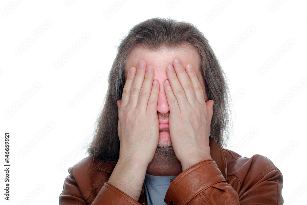 Adult man with long hair covers his eyes with his hands. Adult man with long hair covers his eyes with his hands.