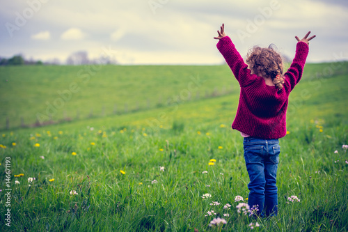 une fillette levant les bras devant un grand pré 