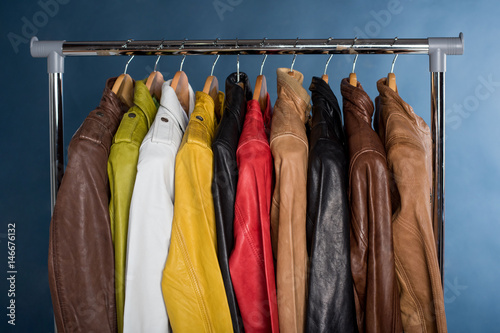 Different color leather jacket hanging on rack on blue background