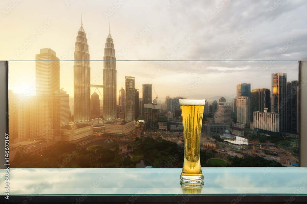 Naklejka premium Piwo i piwo piankowe na stole w barze na dachu z wieżowca Kuala Lumpur w tle w Kuala Lumpur, Malezja.
