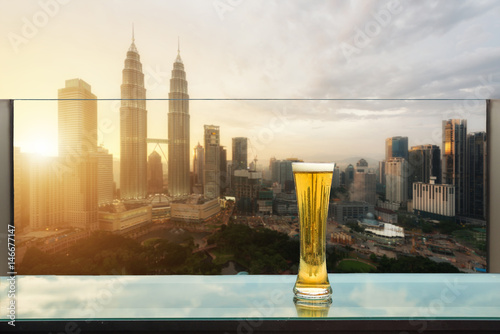 Beer and foam beer on table in rooftop bar with Kuala Lumpur skyscraper in background in Kuala Lumpur, Malaysia.