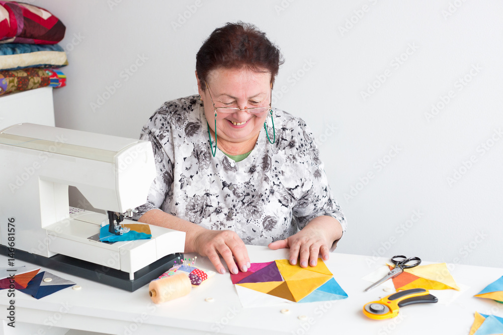 needlework and quilting in the workshop of a tailor woman - elderly smiling women put on the desktop the pieces of colored tissue, lay next to the scissors, buttons, pins and thread, rotary cutters needlework and quilting in the workshop of a tailor woman - elderly smiling women put on the desktop the pieces of colored tissue, lay next to the scissors, buttons, pins and thread, rotary cutters