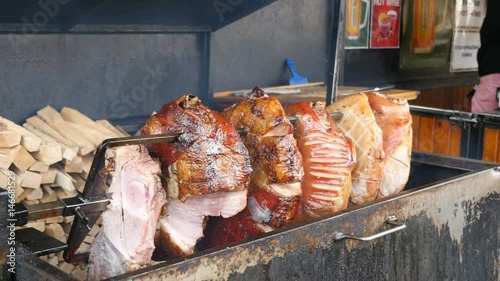 Rotisserie roasting of meat skewered on a spit and rotated horizontaly over charcoal placed in a big metal brazier. The roasted meat looks delicious and juicy in a sunny day in spring photo