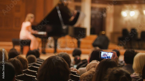 Spectators in concert hall during performing piano girl- people shooting performance on smartphone photo