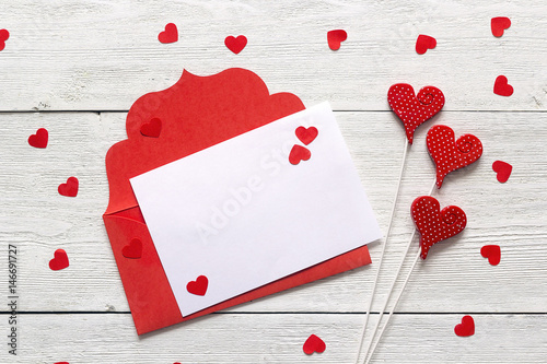 Red envelope with blank card and hearts on white wooden background. Copy space, top view. © WindyNight