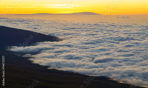 The hillside of the teide volcano lit by the setting sun  down the ocean and flowing sea of clouds