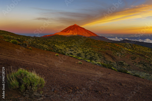 The hillside of the teide volcano lit by the setting sun, down the ocean and flowing sea of clouds