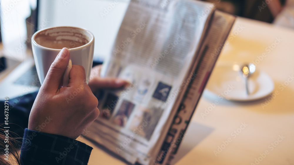 A business woman reading newspaper and drinking coffee in the morning in office - obrazy, fototapety, plakaty 