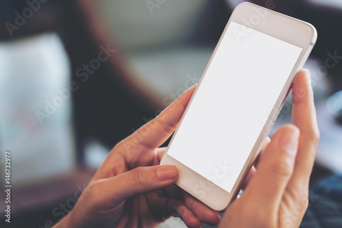 Mockup image of hand holding mobile phone with blank white screen in vintage cafe