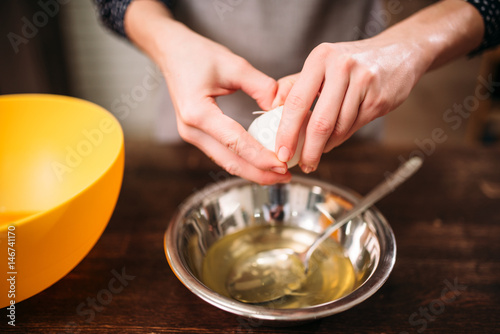 Female hands breaks the egg into a bowl