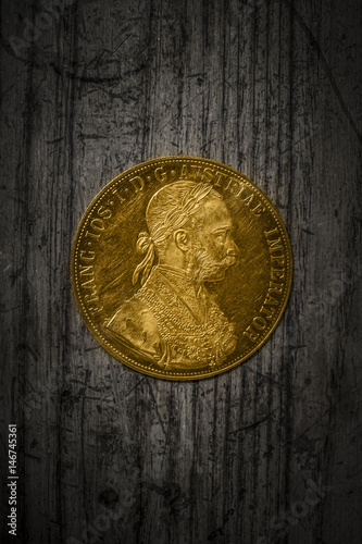Close-up view of Austria-Hungary thaler, avers of golden coin-ducat from 1915 with Kaiser Franz Joseph I on dark wooden background