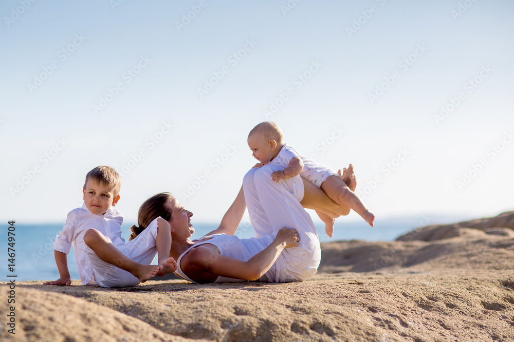 A mother and two sons are doing yoga exercises at the seashore of Mediterranean sea A mother and two sons are doing yoga exercises at the seashore of Mediterranean sea