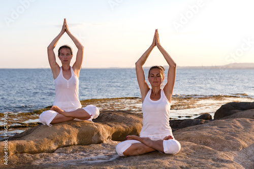 Two sisters are doing yoga exercises at the seashore of Mediterranean sea