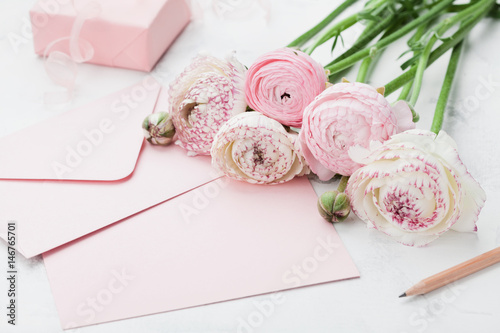 Fototapeta Naklejka Na Ścianę i Meble -  Envelope or letter, paper card, gift and pink ranunculus flowers on white table for greeting on Mother or Woman Day. Can be used as wedding mockup.