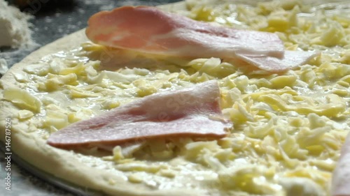 Cooking pizza. Grated cheese and slices of ham on the raw pizza. Close-up. Slow motion. photo