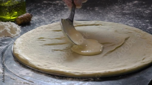 Cooking pizza. Hands adding fresh white sauce to pizza dough. Pizza ingredients on the floured wooden table. Slow motion. photo