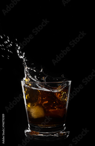 A glass of whiskey and ice cube on a black background