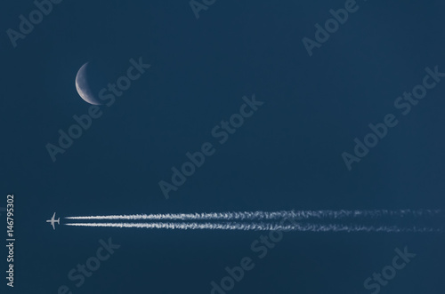 Crescent moon on the night sky near chemtrails from airplane; soft focus photo
